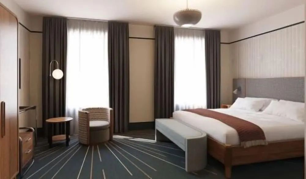 Ein eingerichtetes Hotelzimmer mit Doppelbett, gepolsterter Bank und Sessel vor dem Fenster.