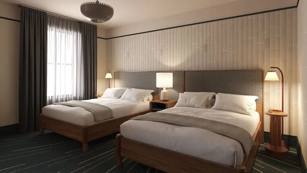 Hotelzimmer mit zwei großen Doppelbetten, Nachttisch mit Lampe und hellem Kopfteil.
