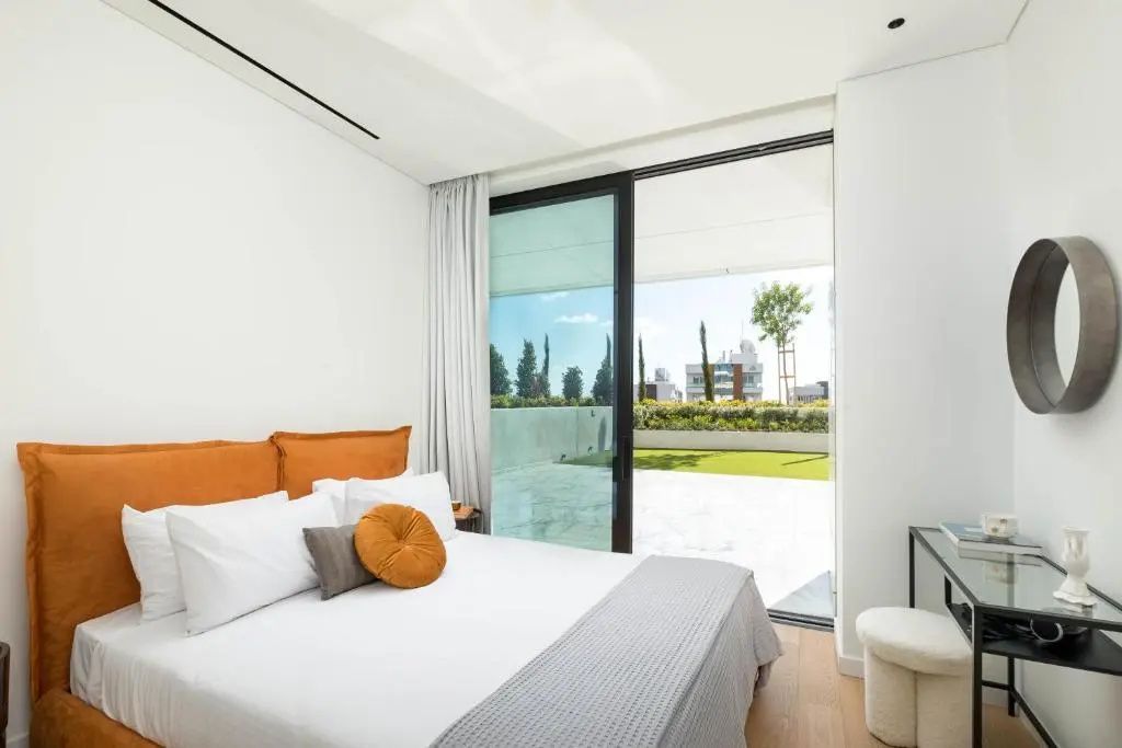 Helles Schlafzimmer mit Doppelbett und großer Glasfront mit Zugang zur Terrasse.