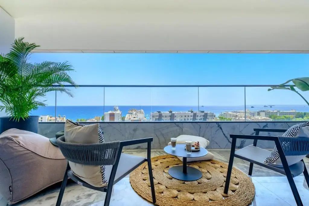 Balkon mit Glasgeländer, Sitzmöbeln und freiem Blick auf das Meer und die Stadt.