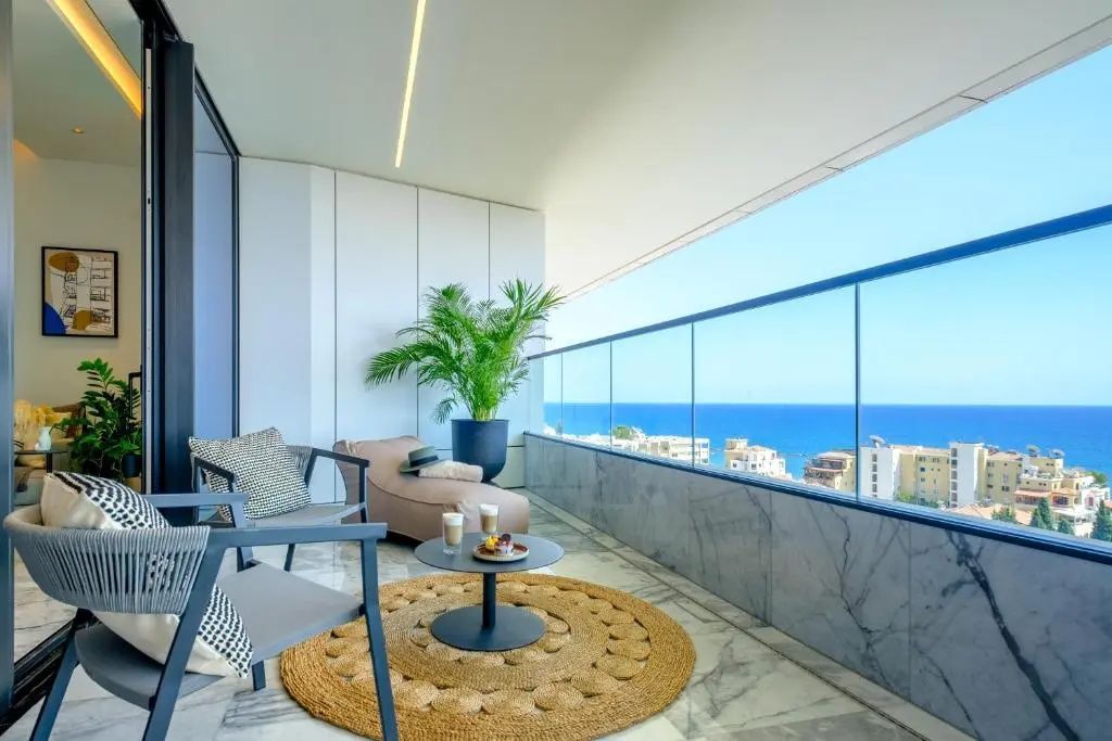Überdachter Balkon mit Liegestuhl, kleinen Tischen und Ausblick auf das Meer.