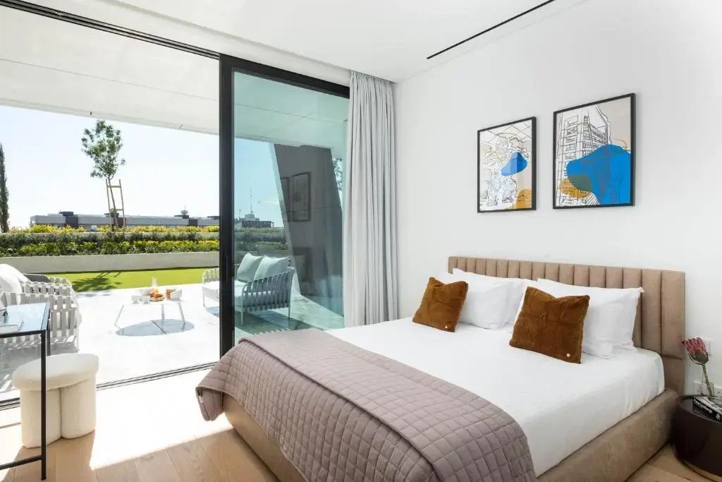 Schlafzimmer mit weißem Doppelbett und geöffneter Glastür zur Terrasse.