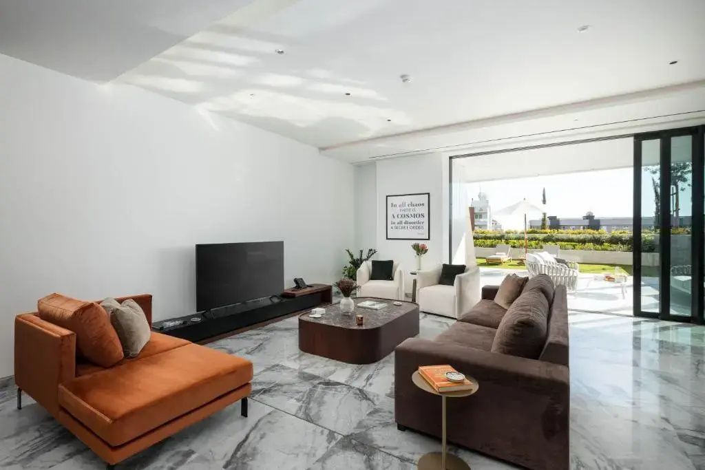 Geräumiges Wohnzimmer mit braunem Sofa, Fernseher und großen Glastüren zur Terrasse.