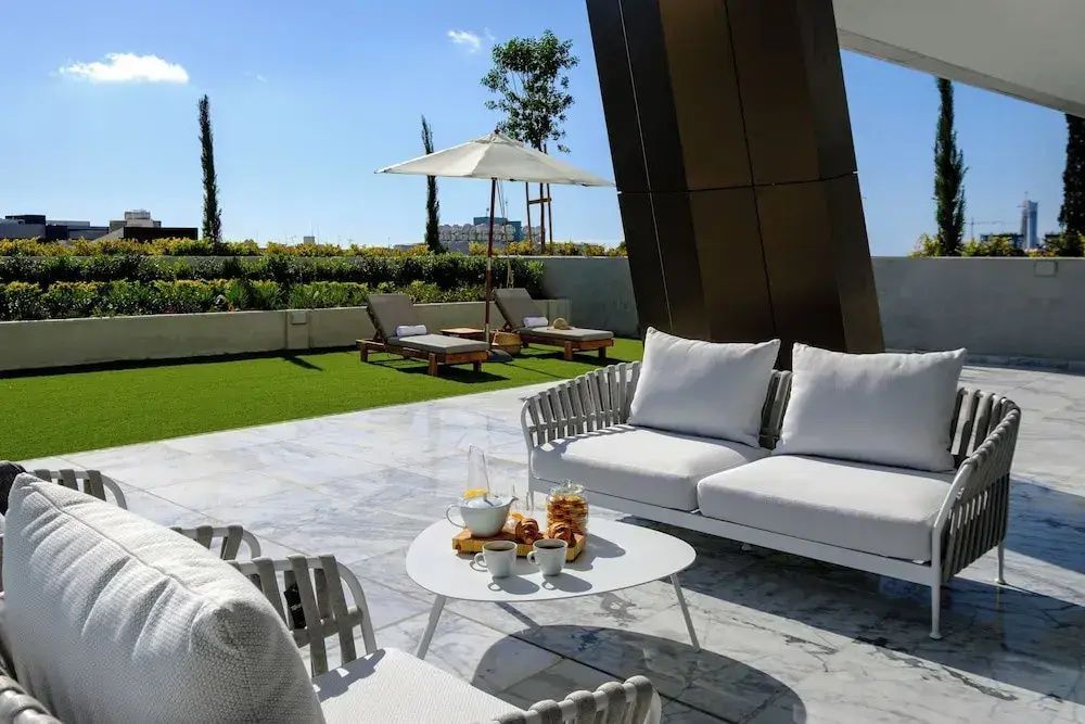 Terrasse mit weißer Sitzgruppe, Beistelltisch sowie Liegestühlen und Sonnenschirm im Hintergrund.