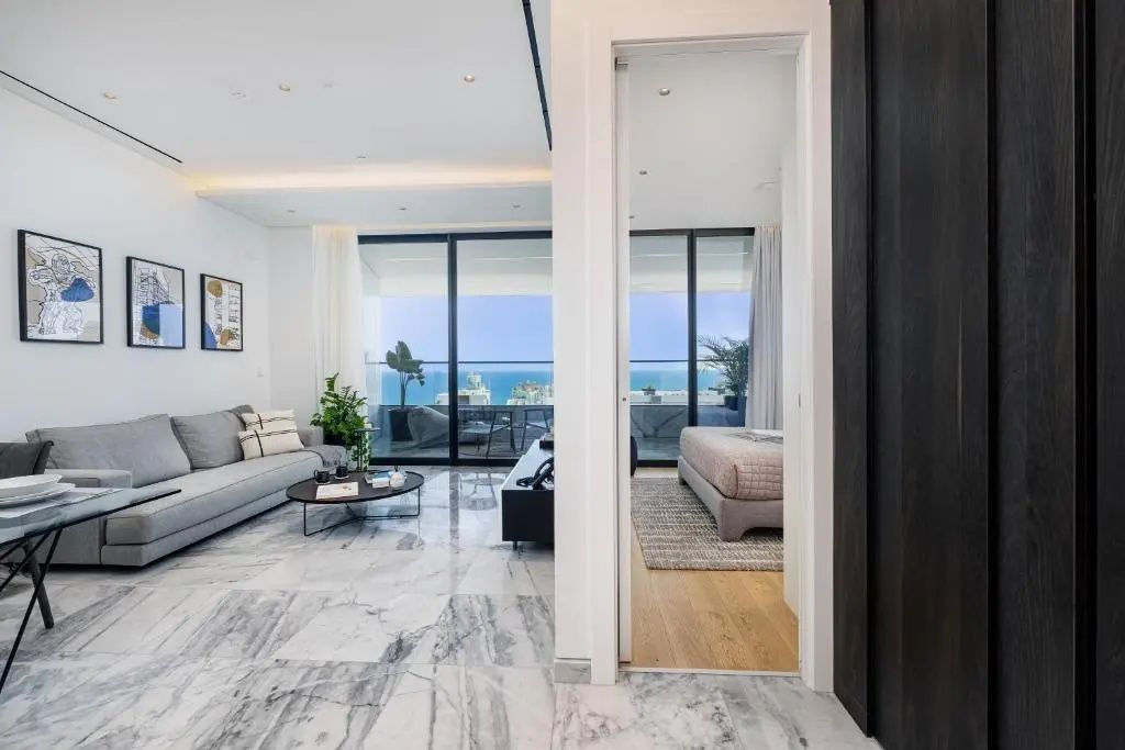Helles Wohnzimmer mit Marmorboden, grauem Sofa und Blick durch große Glastüren auf das Meer.