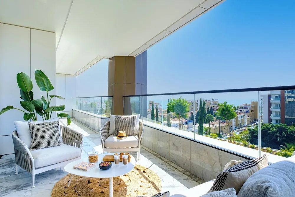 Überdachter Balkon mit Sesseln, einem Tisch und Blick auf die Stadt.