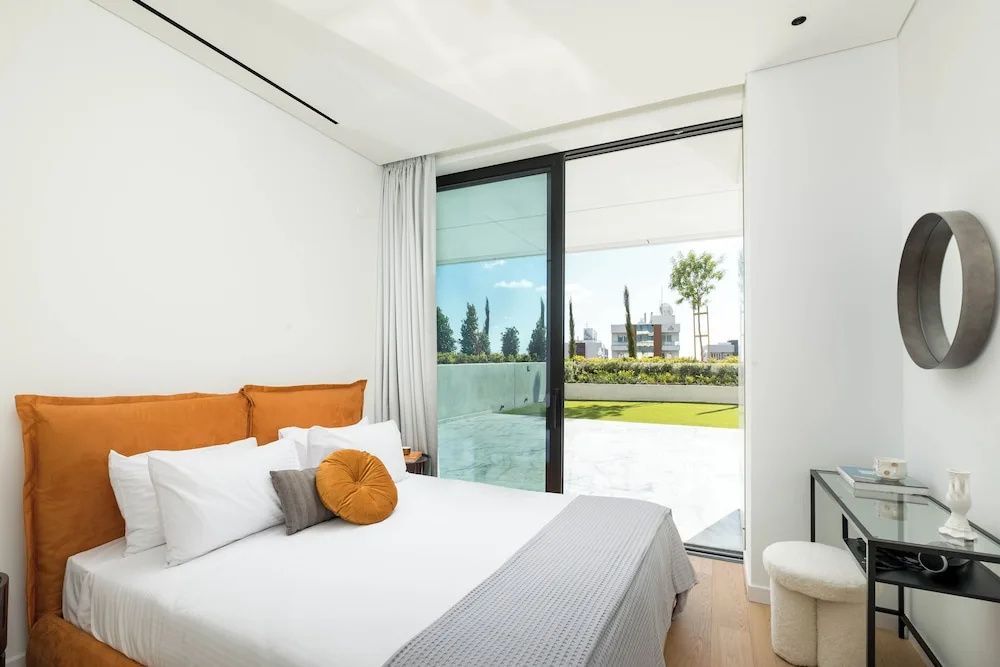 Modernes Schlafzimmer mit Kissen, Parkettboden und Blick auf eine Terrasse mit Rasen.