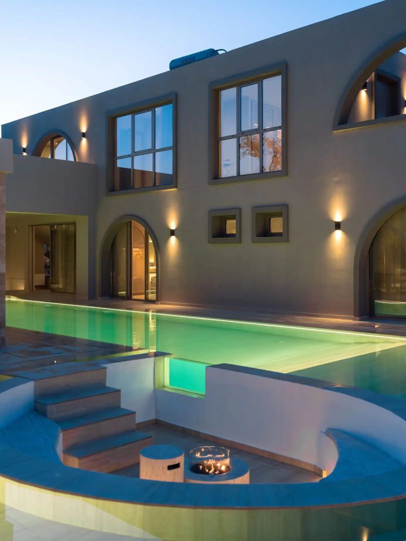 Beleuchtete Fassade der Villa am Abend mit Swimmingpool und Rundbogenfenstern.