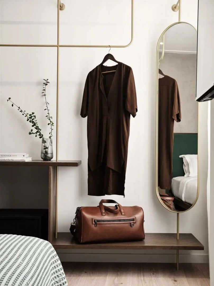 Offenes Regalsystem mit hängender Kleidung, brauner Ledertasche und ovalem Wandspiegel.