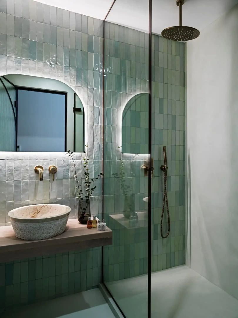 Badezimmer mit grün gefliesten Wänden, Aufsatzwaschbecken aus Stein und beleuchtetem Spiegel.