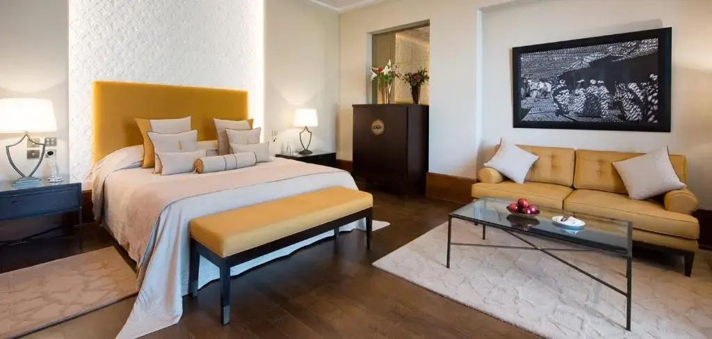 Doppelbett mit gepolsterter Bank davor sowie ein dunkler Schrank mit Blumenstrauß.