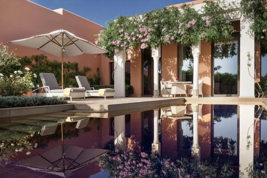 Privater Außenpool mit Wasserspiegelung, zwei Liegestühlen und rosa Fassade mit Kletterpflanzen.