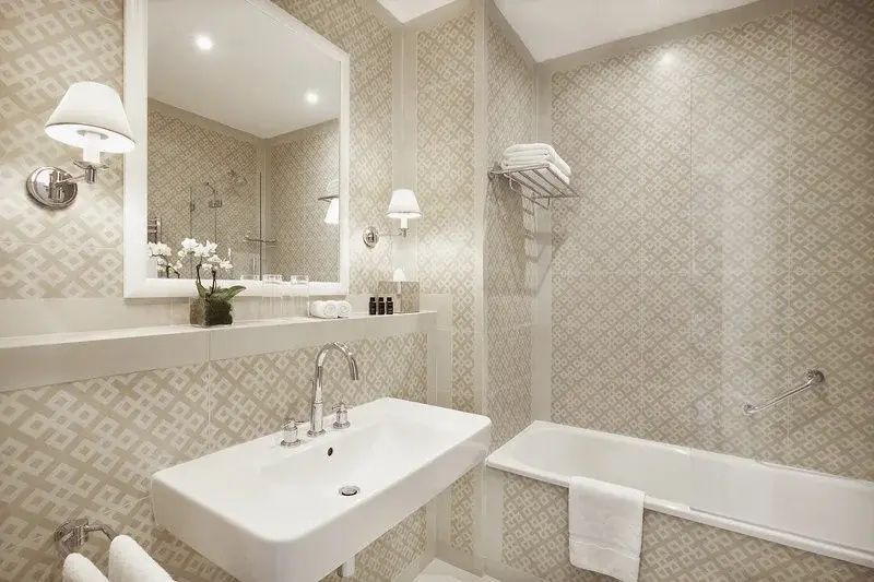 Hell gefliestes Badezimmer mit weißem Waschbecken, Spiegel und eingebauter Badewanne.