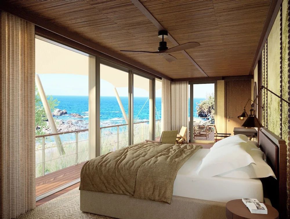 Schlafbereich mit großem Bett und bodentiefen Fenstern mit Blick auf das Meer.