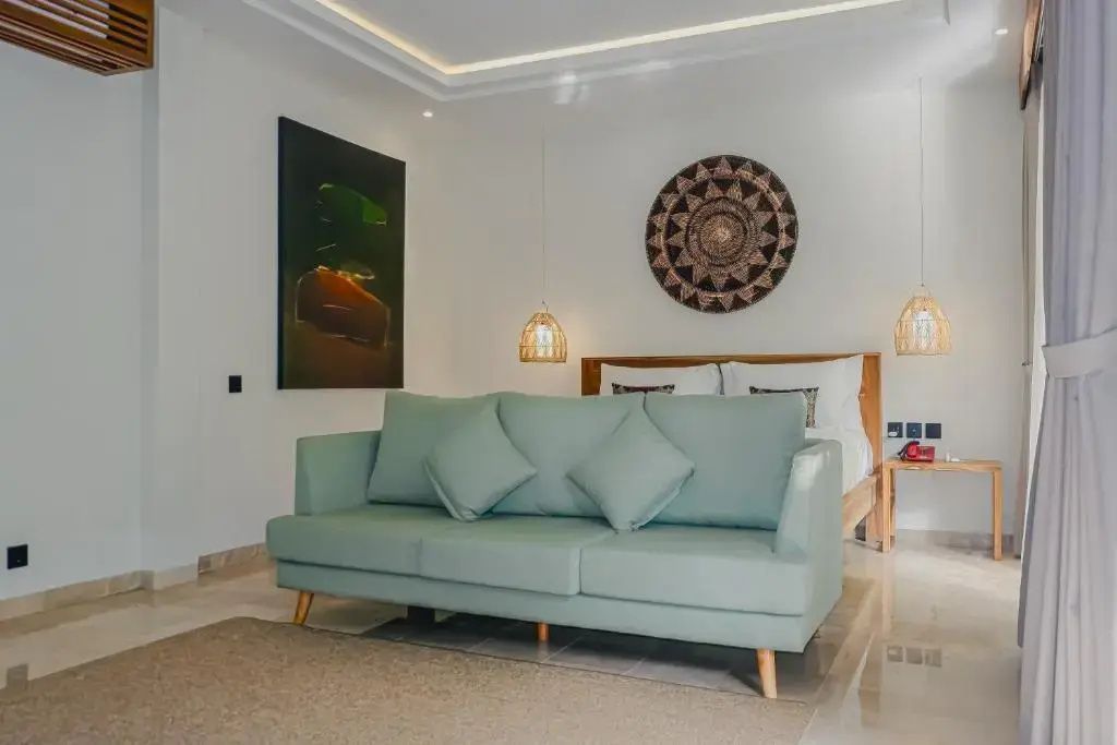 Schlafzimmer mit hellgrünem Sofa im Vordergrund, Doppelbett im Hintergrund und Wandschmuck.