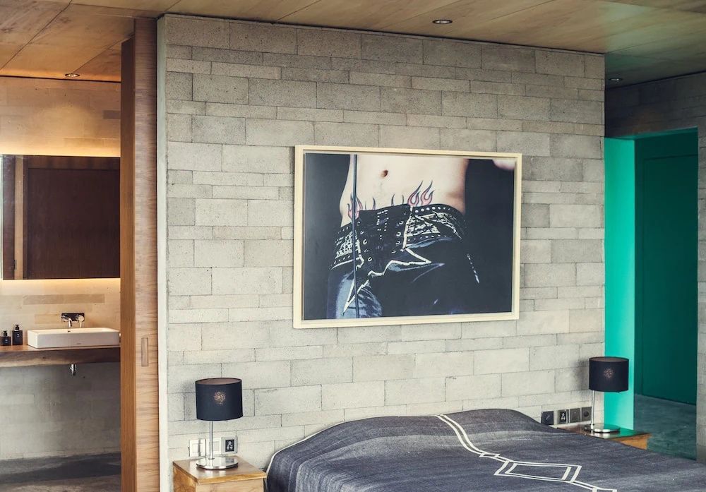 Doppelbett mit gemusterter Tagesdecke vor einer grauen Steinwand mit Kunstwerk.