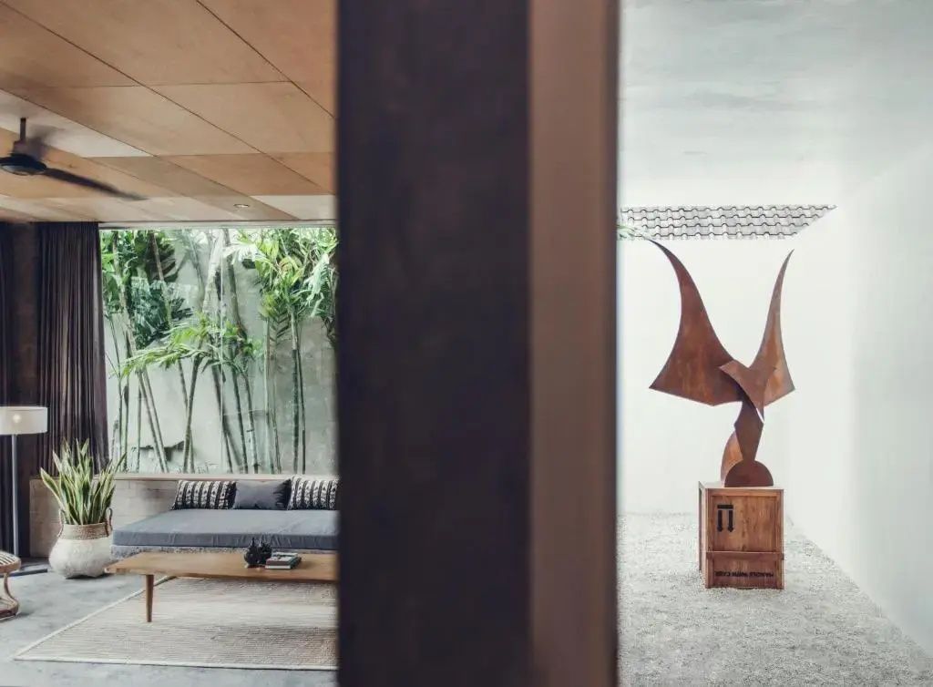 Ein moderner Wohnbereich mit grauer Sitzbank, Holzcouchtisch und einer Holzskulptur im Raum.