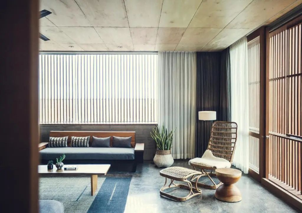 Geräumiger Wohnbereich mit grauer Couch, Flechtsessel, Holzdecken und großem Fensterfront-Element.
