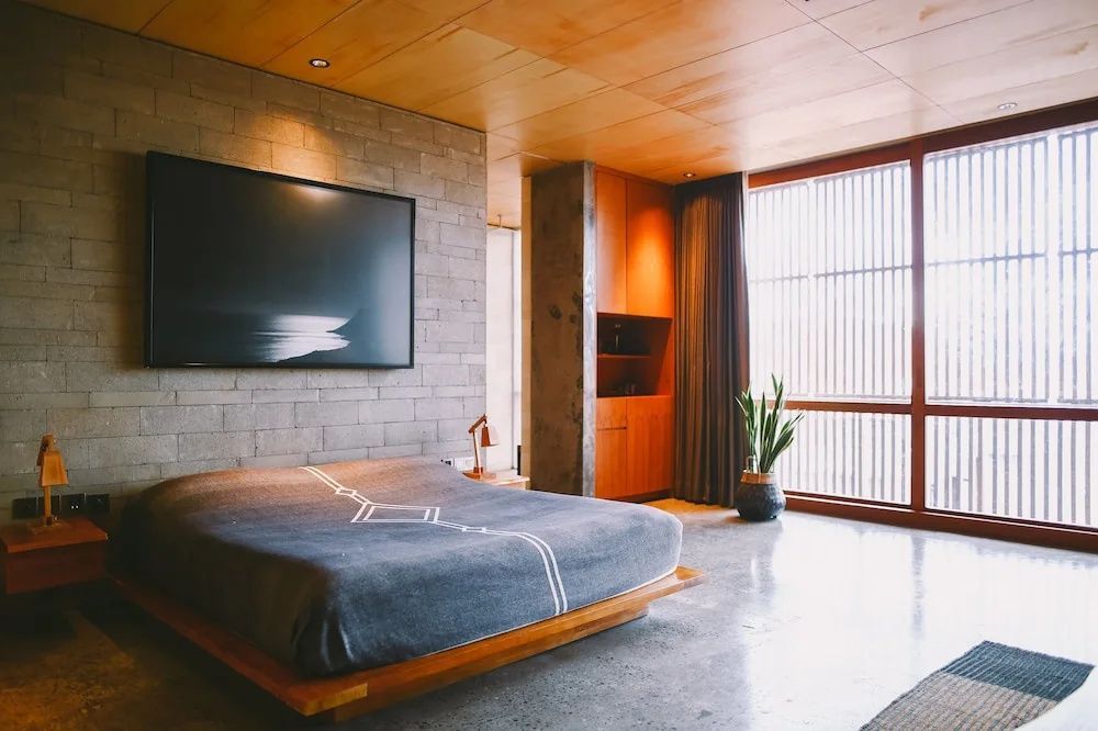 Schlafzimmer mit großem Bett, Wandbild auf Backsteinwand und Holzverkleidungen.