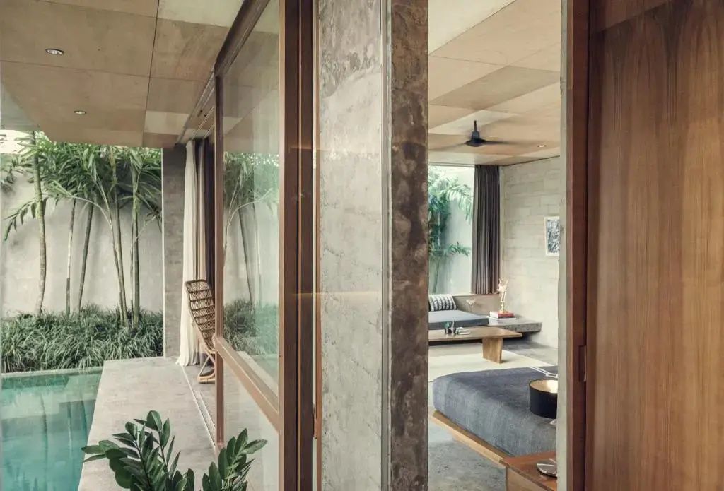 Blick durch geöffnete Schiebetüren in ein Hotelzimmer mit Bett, Sofa und Betonelementen.