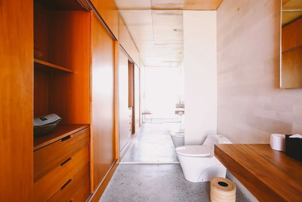 Badezimmerbereich mit Toilette, Holzschränken und hellem Betonboden.