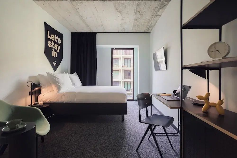 Modernes Hotelzimmer mit einem Doppelbett, Schreibtisch und einer Sichtbetondecke.