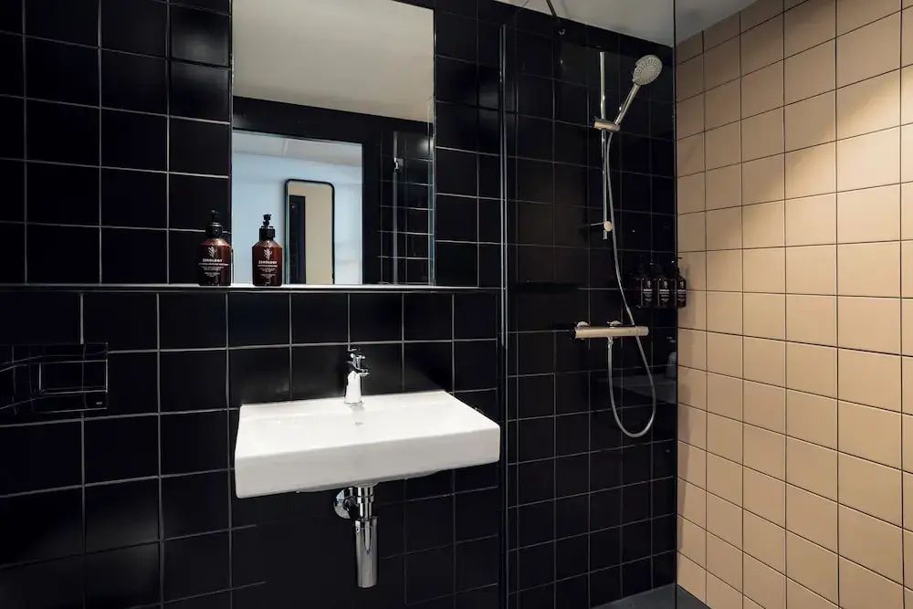 Badezimmer mit schwarzen Wandfliesen, weißem Waschbecken und einer Dusche mit Glaswand.