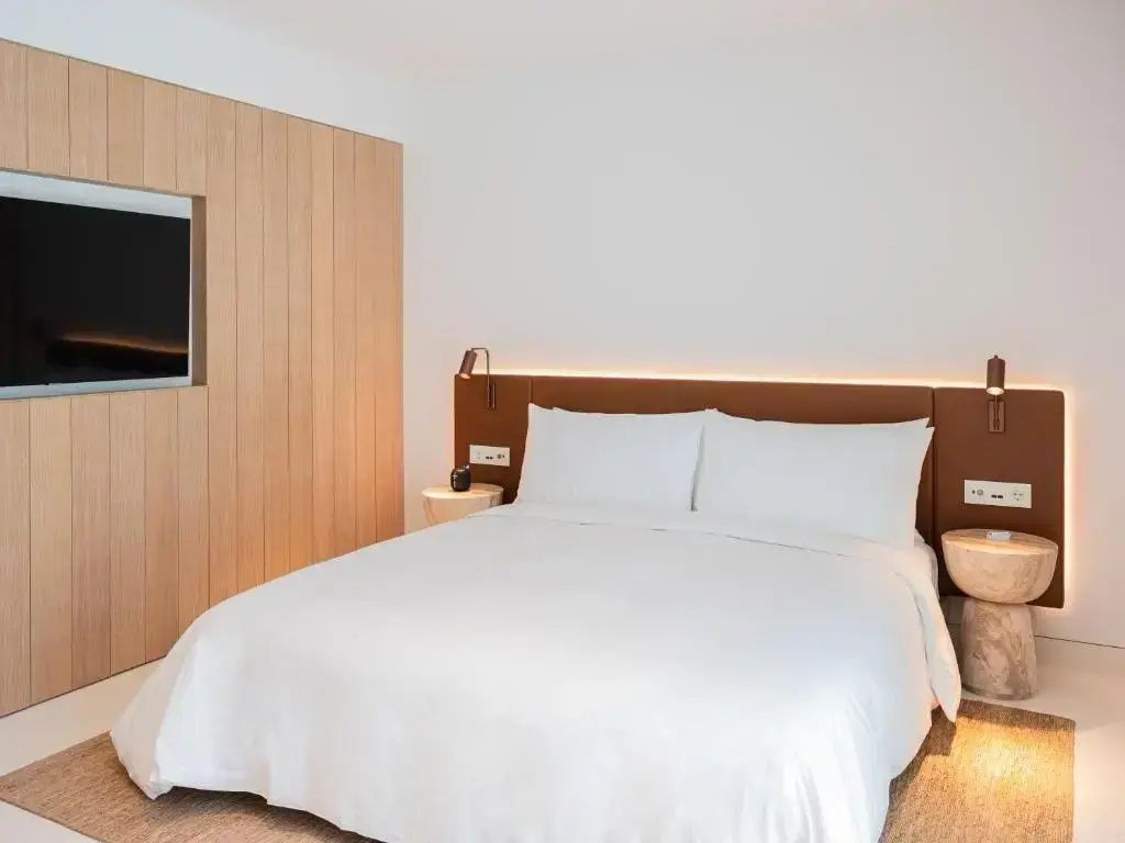 Doppelbett mit weißer Bettwäsche, braunem Kopfteil und Holzverkleidung an der Wand.