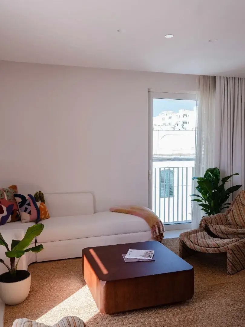 Wohnbereich mit weißem Sofa, Sessel, Couchtisch und Balkontür in einem Hotelzimmer.