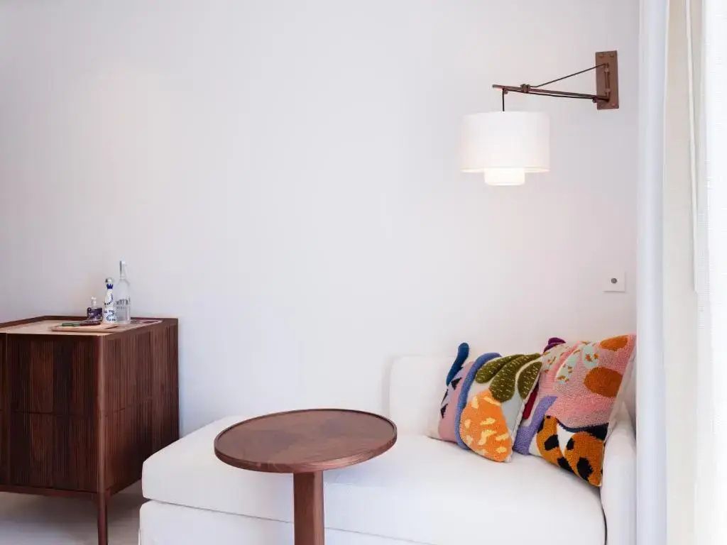 Weißes Sofa mit bunten Kissen und einem kleinen runden Holztisch in einer Zimmerecke.