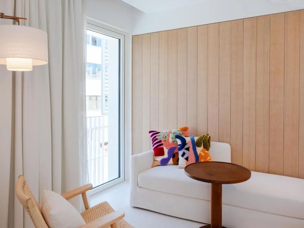 Sitzecke im Zimmer mit weißem Sofa, buntem Kissen, Holzstuhl und kleinem runden Holztisch.