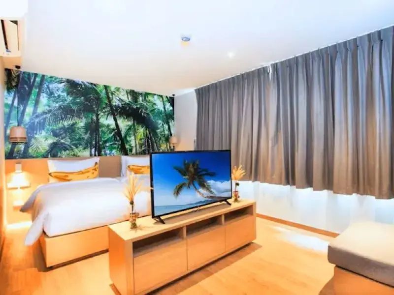 Schlafbereich im Hotelzimmer mit Flachbildfernseher, Bett und grauen Vorhängen am Fenster.