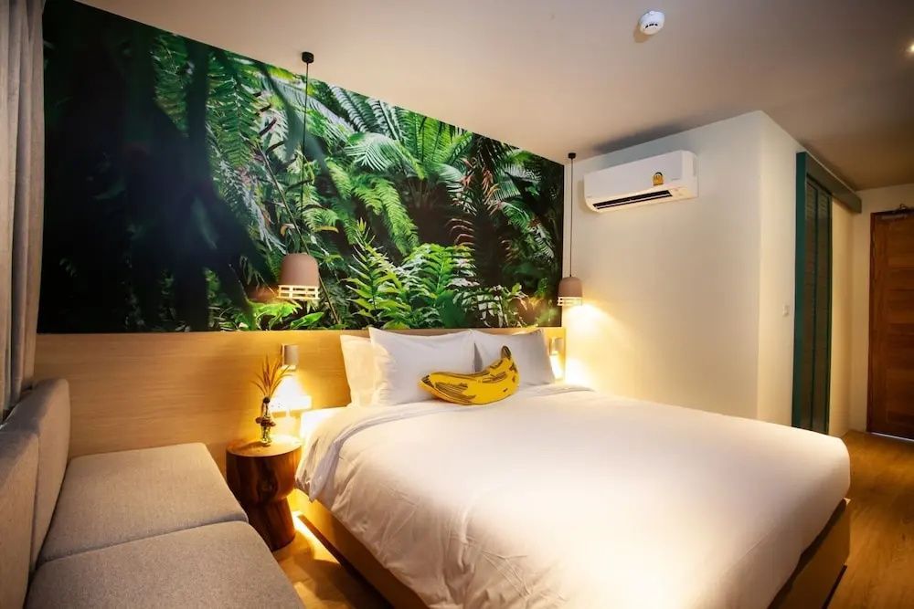 Doppelbett mit gelbem Kissen und grüner Wandgestaltung im hellen Hotelzimmer.