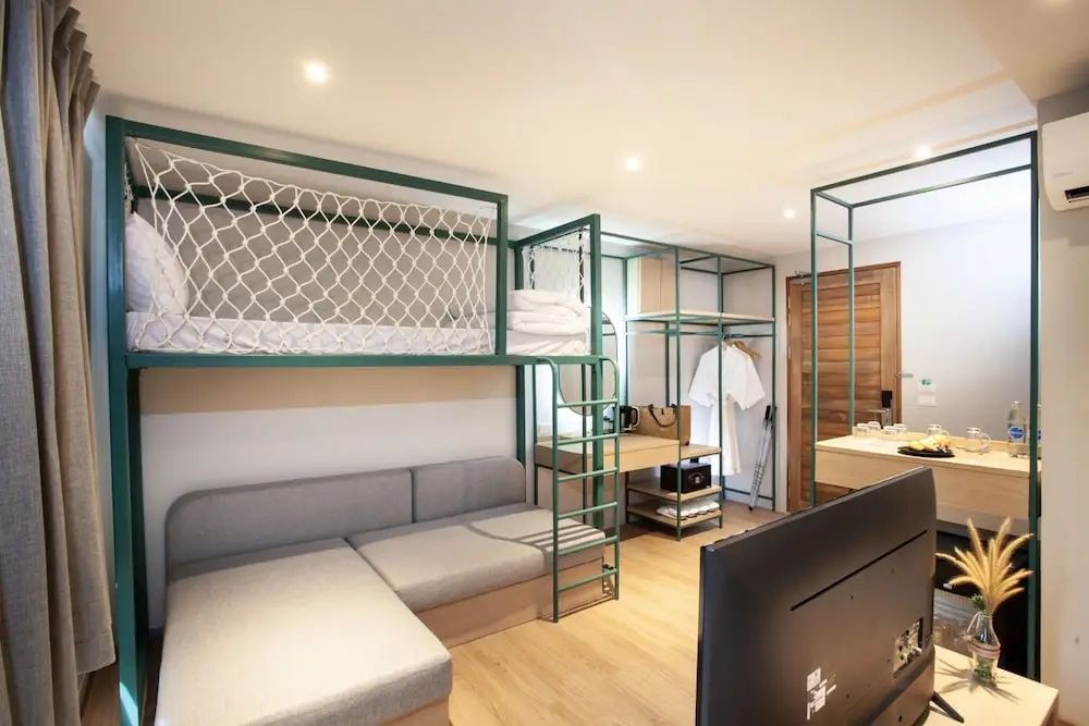 Sitzbereich mit grauem Ecksofa, grüner Metallkonstruktion für ein Etagenbett und Holzfußboden.
