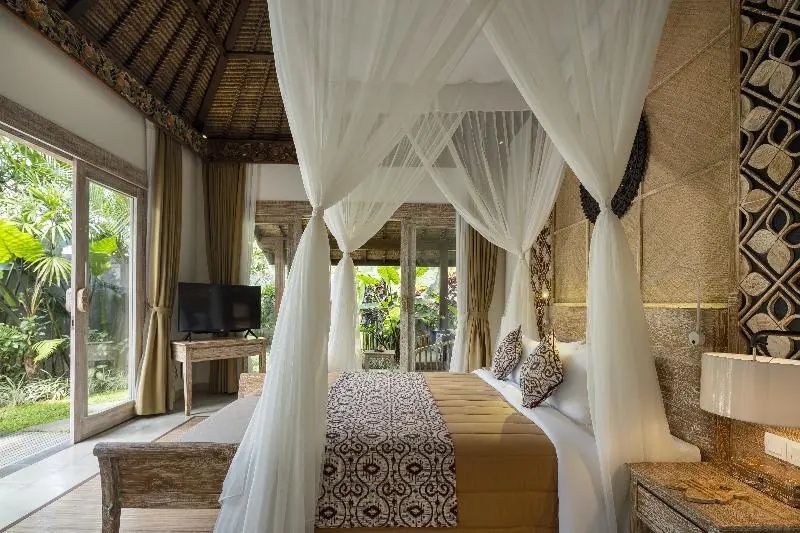 Schlafzimmer einer Villa mit Doppelbett, weißem Moskitonetz und Blick auf tropische Pflanzen.