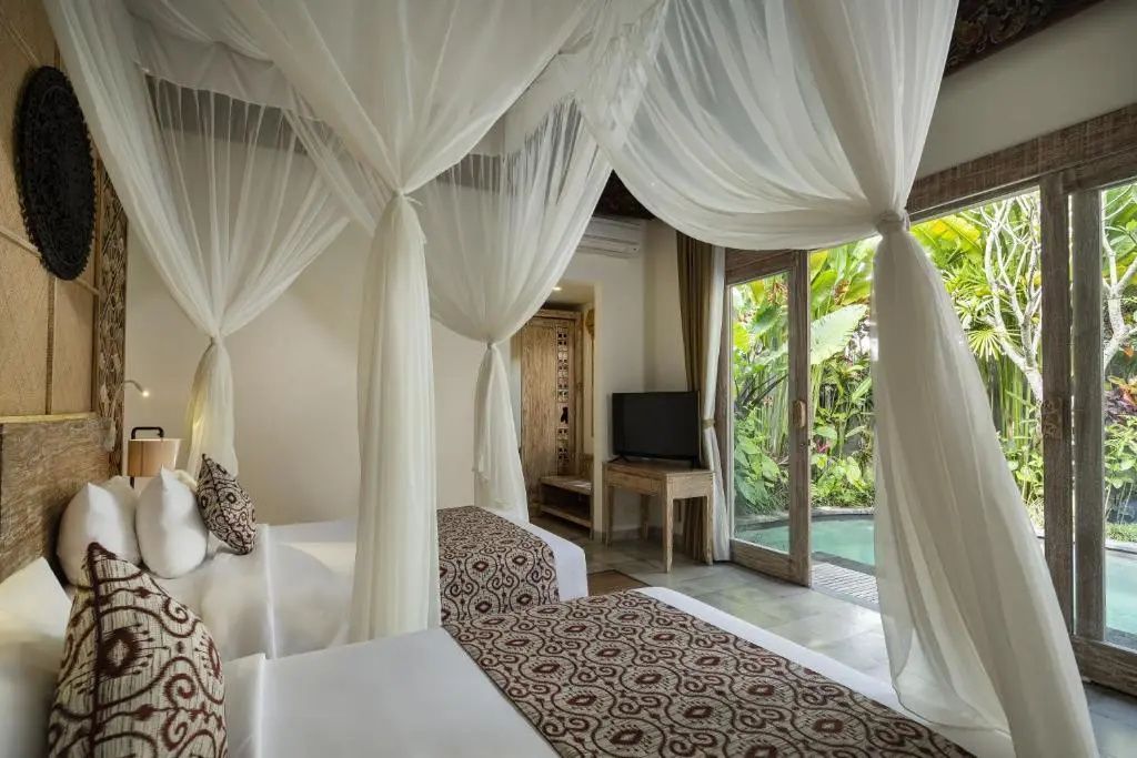 Schlafzimmer mit zwei Einzelbetten unter weißen Moskitonetzen und Tür zum Außenbereich.