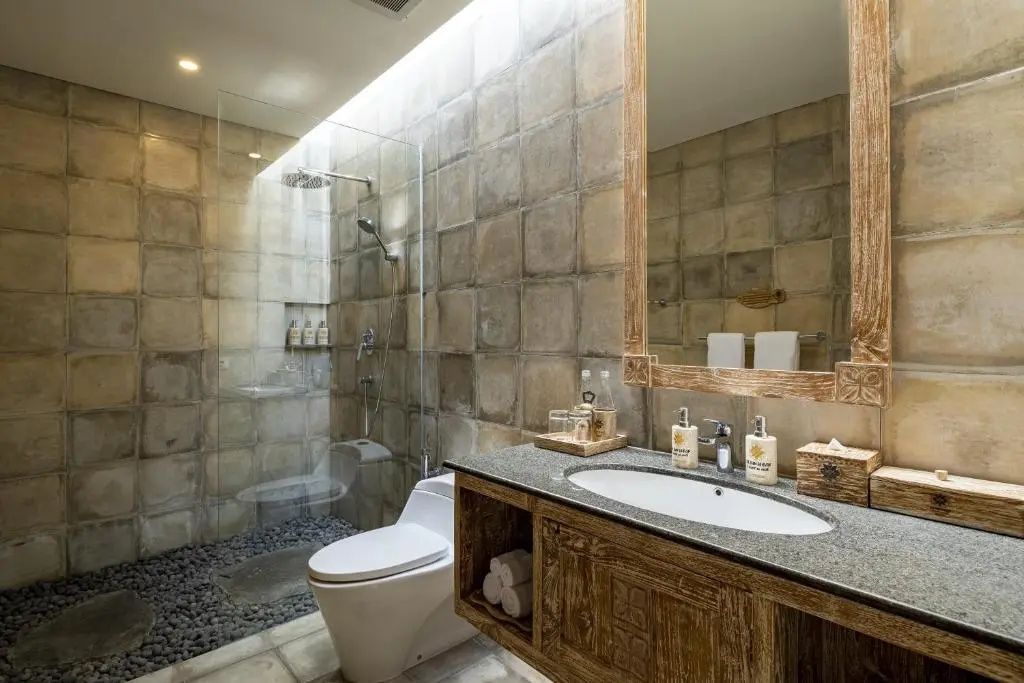 Badezimmer mit Waschtisch aus Holz, einer Dusche mit Steinfliesen und Toilette.