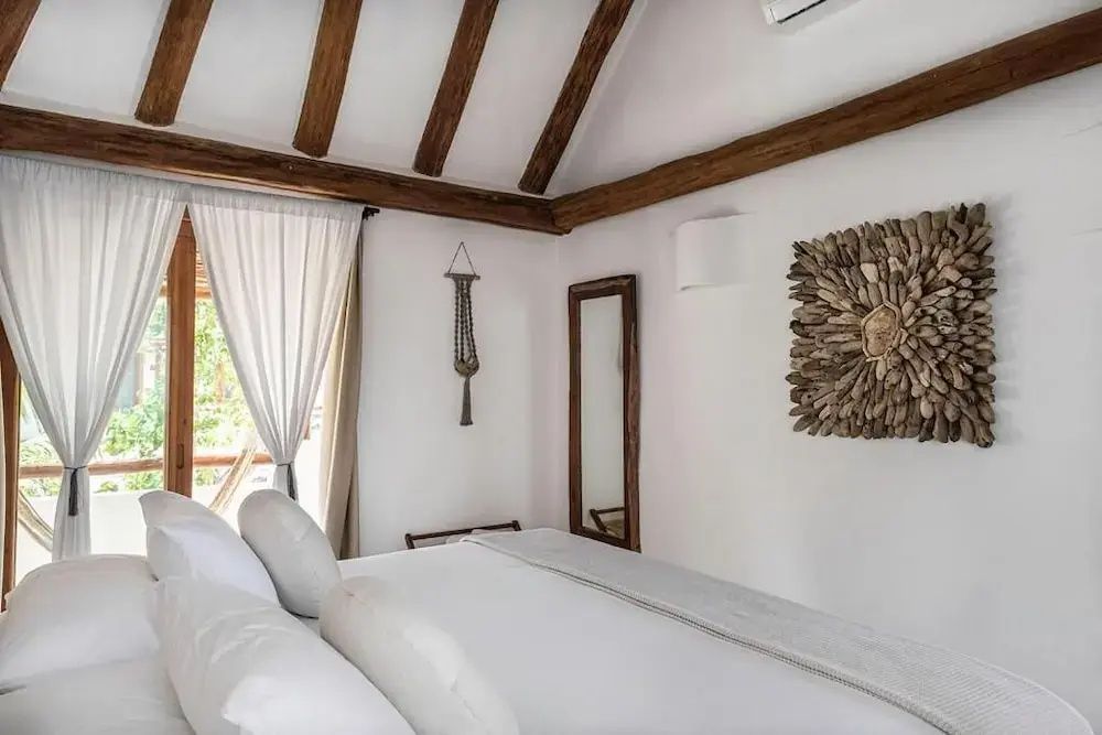 Schlafbereich mit Doppelbett, Wandspiegel und Holzdekoration an der weißen Wand.
