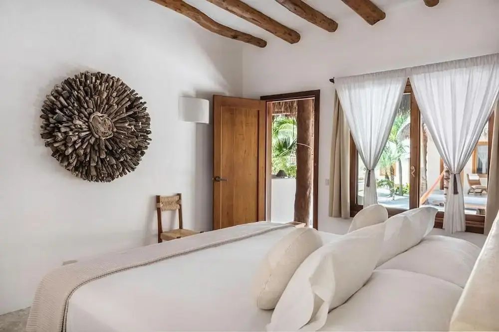 Blick über das Hotelbett zur geöffneten Tür und einer Wanddekoration aus Holz.