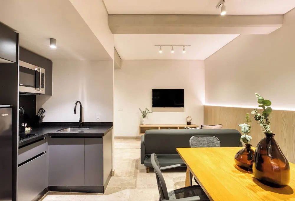 Modern eingerichtetes Wohnzimmer mit kleiner Küchenzeile, Esstisch und Fernseher an der Wand.