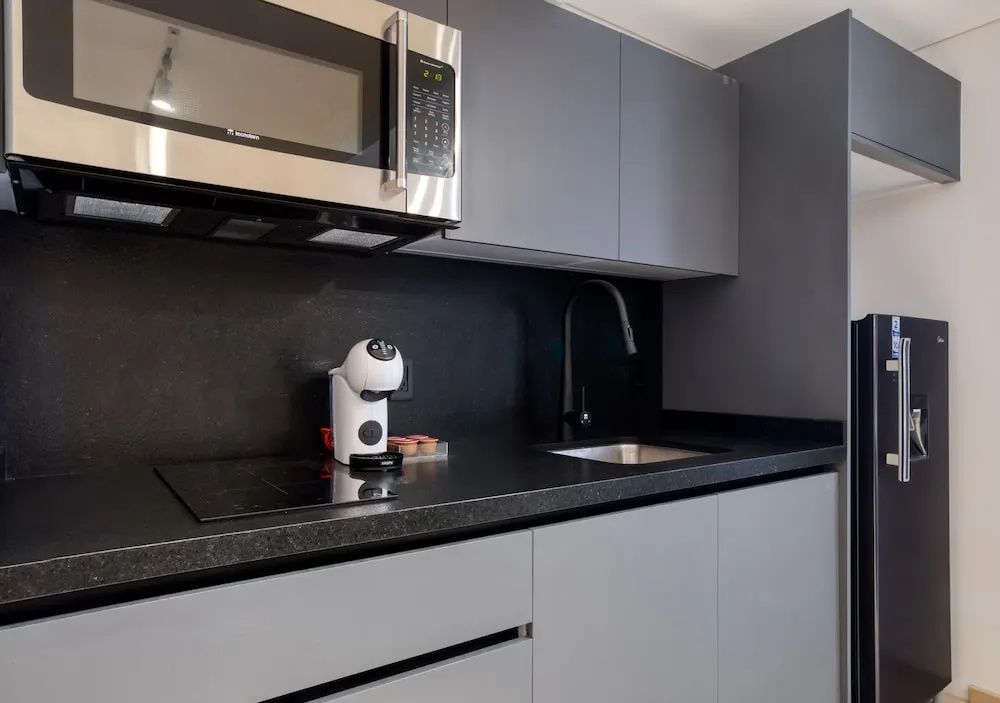 Moderne graue Küchenzeile mit Mikrowelle, Kaffeemaschine, Kochfeld und Spülbecken.