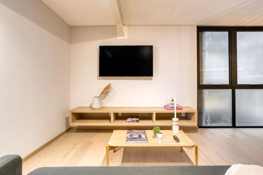 Wohnbereich mit flachem Wandfernseher, langem Holzregal und hellem Holzboden.