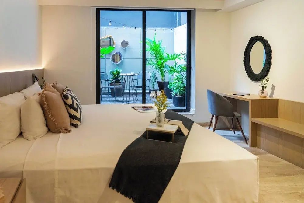 Schlafzimmer mit Doppelbett, Schreibtisch und Blick durch Glasfront auf eine begrünte Terrasse