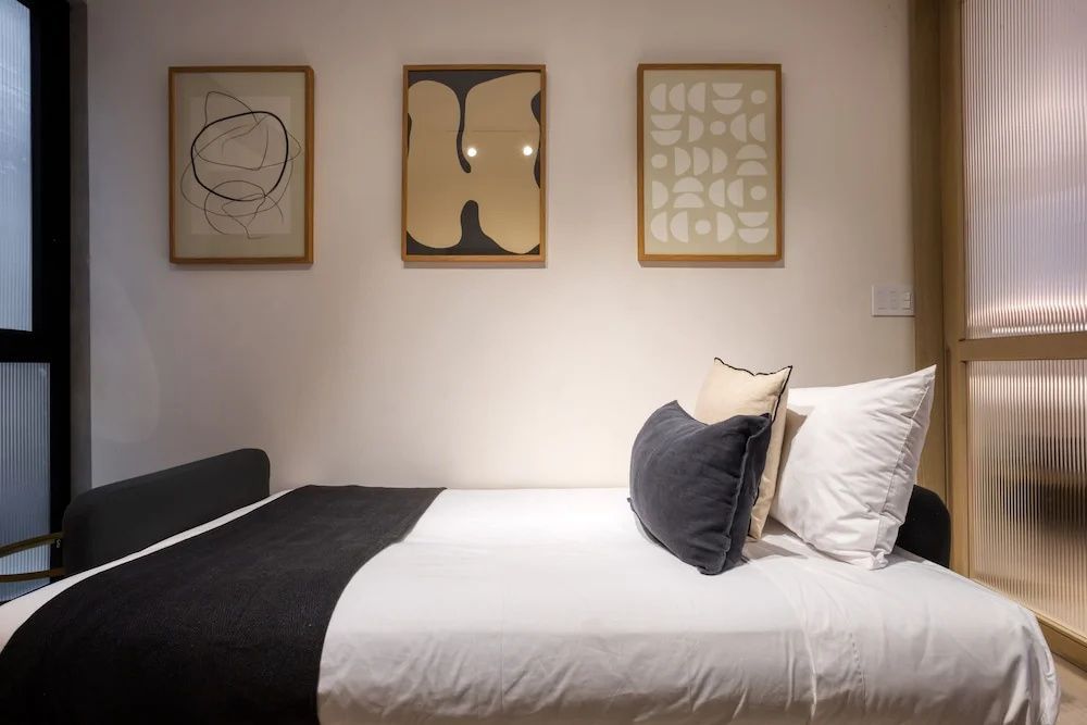 Einzelbett mit weißer Bettwäsche und drei abstrakten Bildern an der Wand.