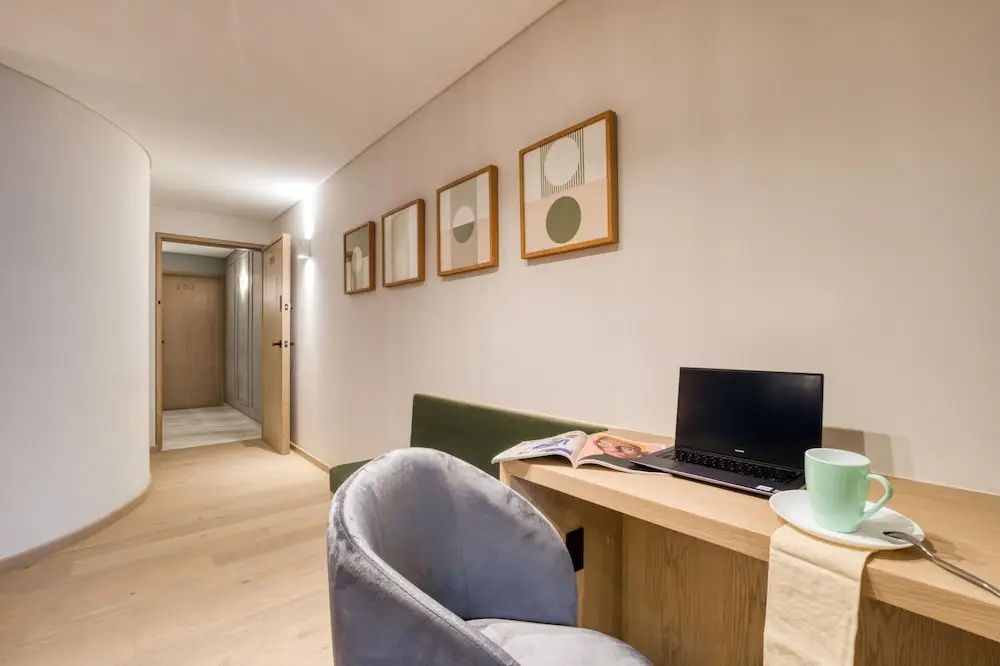 Arbeitsplatz mit Holzschreibtisch, Laptop, Samtsessel und Wandbildern.