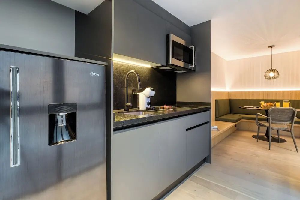 Moderne Küchenzeile mit Kühlschrank, Mikrowelle, Spülbecken und dunklen Fronten.