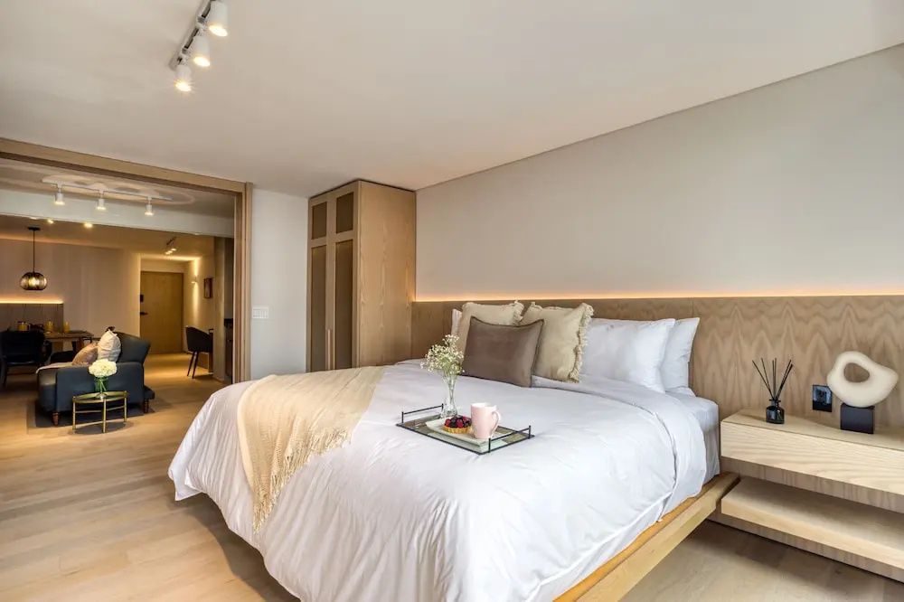 Doppelbett mit hellem Holzkopfteil, Kissen, Decke und Holzschrank.