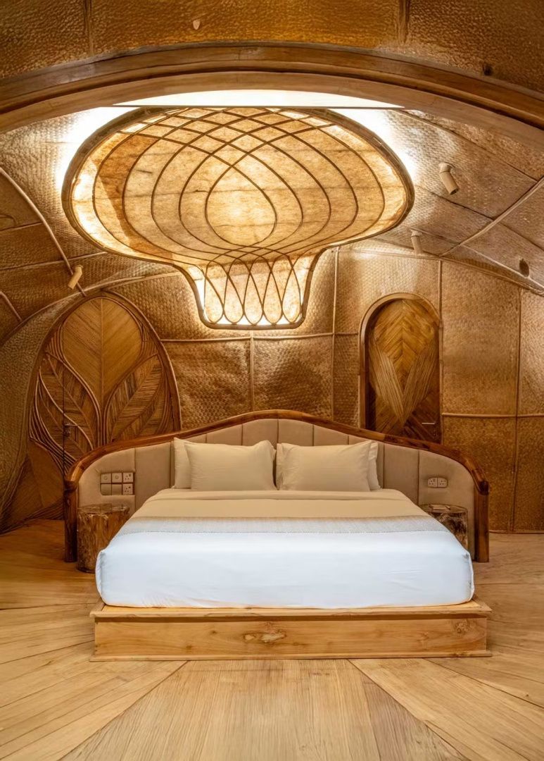 Doppelbett aus Holz mit weißer Bettwäsche in einem Raum aus Bambus mit kunstvoller Deckenbeleuchtung.