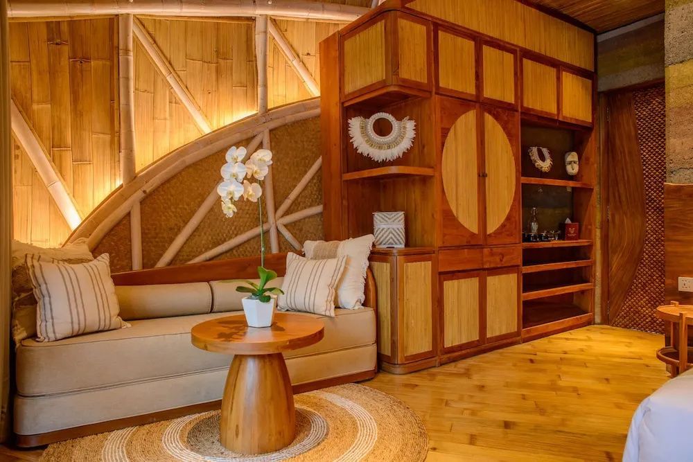 Sitzbereich in einer Unterkunft mit Holzschrank, Sofa, Orchidee auf dem Tisch und Bambuswänden.