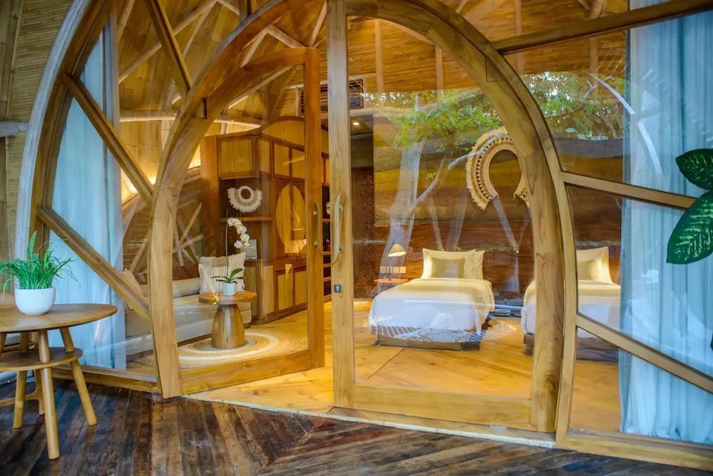 Blick durch eine rundbogige Glastür auf ein Schlafzimmer mit zwei Einzelbetten und Holzmöbeln.